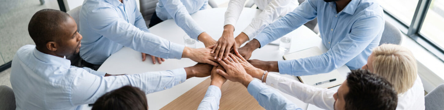 Overhead view of business people stacking their hands together in the center, representing teamwork, unity, collaboration, trust and shared commitment to common goals.