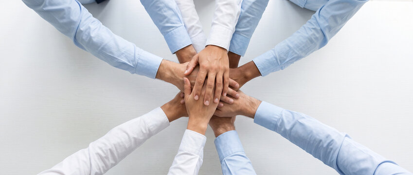 Overhead view of business people stacking their hands together in the center, representing teamwork, unity, collaboration, trust and shared commitment to common goals.