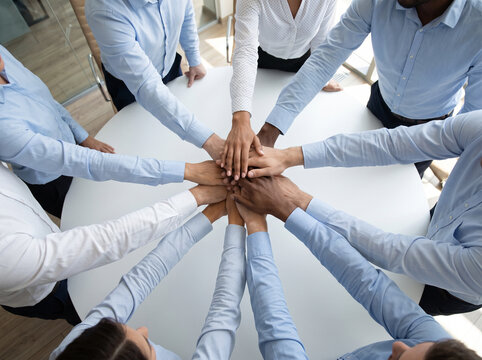 Overhead view of business people stacking their hands together in the center, representing teamwork, unity, collaboration, trust and shared commitment to common goals.