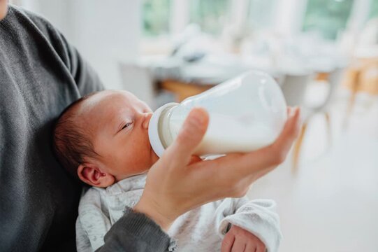 Mother holding and feeding her newborn baby from a bottle in a bright interior