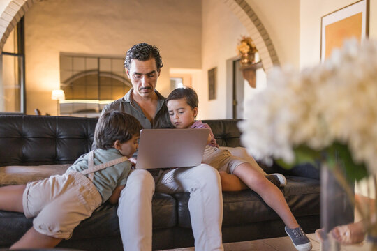 Father using laptop with his two young sons on sofa at home