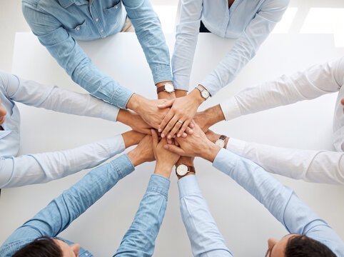 a stack of hands showing unity and teamwork, top-down overhead view of multiple business people placing hands together in the center
