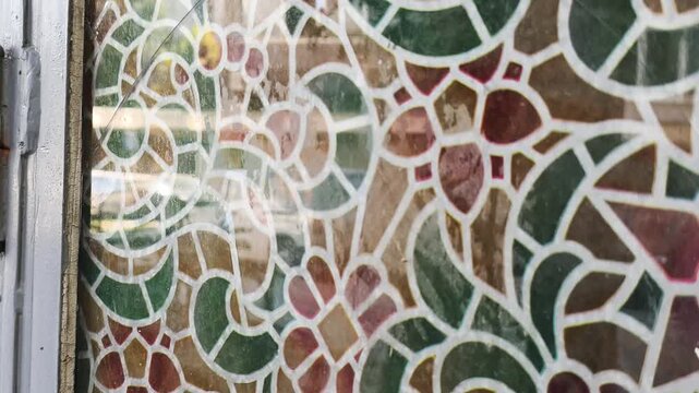 Reflective mosaic glass in vintage building architecture. Decorative mosaic glass window pattern reflects urban street movement, creating unique historical texture and creative background.