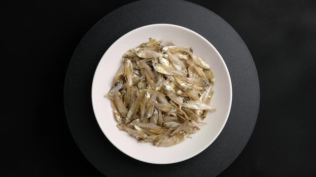Dried Thai river sprat in white plate or Dried glass minnow (pla siu kaew).a tiny, see-through freshwater fish that is dried in the sun.Top view.