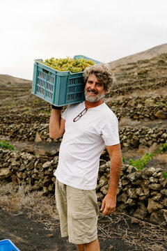 Man holding a crate of organic green grapes and looking at camera.