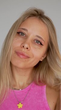 Young blonde woman sends an air kiss with her hand, showing playful flirty mood on light background