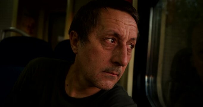 Moody portrait of a serious man commuting on a train in low light. Concept of quiet introspection, tired commuting, emotional journeys, and evening transit. 4K.