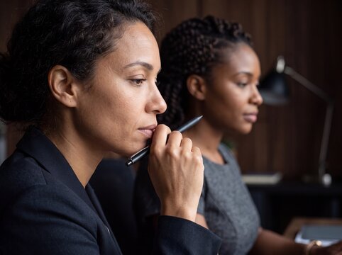 Two professional women in a Q&A session focusing thoughtfully with stylus pen and soft diffused lighting in office