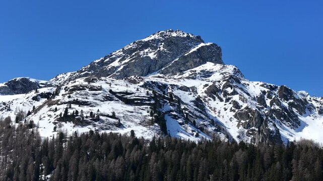 rocky pyramidal summit crowns snowcapped peak towers above dense larch pine forest slow push in aerial drone footage julier pass mountain pass graubunden switzerland swiss alps high altitude