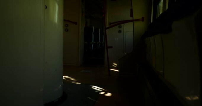 Low key interior shot of bright sunlight pools cast across the floor of a dark train vestibule. 4K.