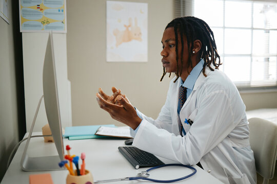 Young adult African American male pediatrician consulting online via computer in clinic. Concept representing telemedicine and pediatric healthcare communication