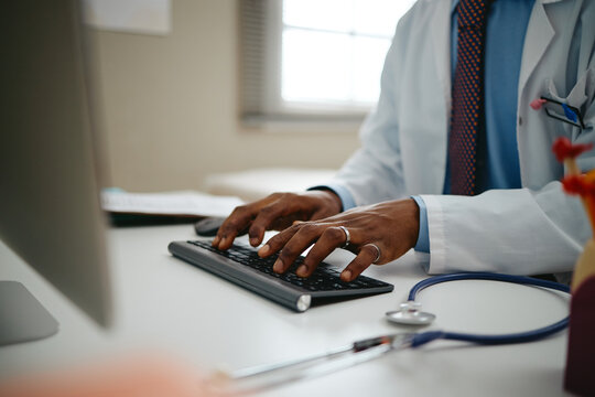 African American male pediatrician typing on computer keyboard near stethoscope in clinic. Visual suitable for digital healthcare software and medical advertising