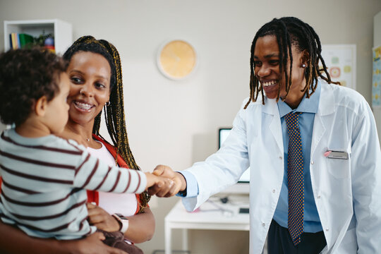 African American doctor shaking hands with toddler child held by mother during pediatric checkup in clinic. Ideal visual asset for family healthcare campaigns, pediatric medicine websites