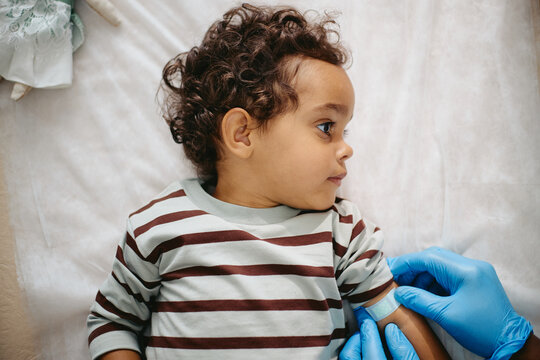 African American toddler receiving adhesive bandage on arm from pediatrician after vaccination. Perfect for pediatric healthcare campaigns and child immunization advertising