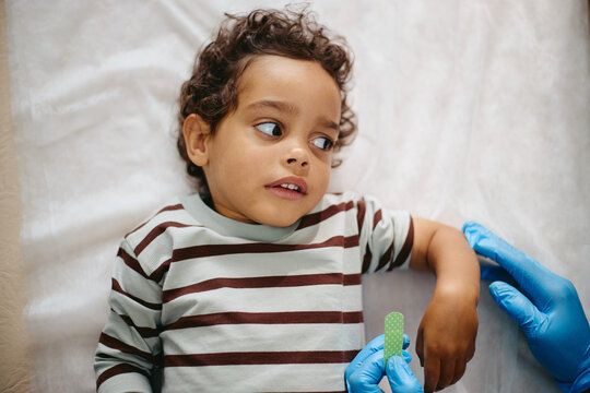 African American toddler boy lying down while pediatrician applying adhesive bandage on arm after vaccination. Useful for pediatric healthcare and vaccination campaigns