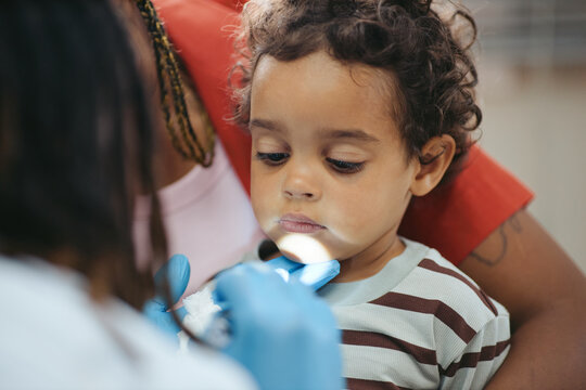 African American toddler child receiving medical throat checkup from doctor in gloves during clinic visit with mother. Scene suitable for pediatric healthcare and insurance advertising