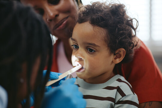 African American pediatrician examining throat of African American toddler held by mother during medical checkup. Useful for pediatric healthcare campaigns and family medicine promotion