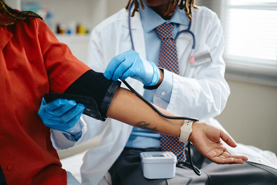 African American doctor measuring blood pressure of young adult African American patient during medical checkup. Concept represents pediatric healthcare, cardiology diagnostic, clinical exam