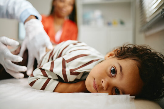 Portrait of African American child lying on exam table during pediatrician checkup with mother. Ideal visual for pediatric clinic advertising and healthcare marketing