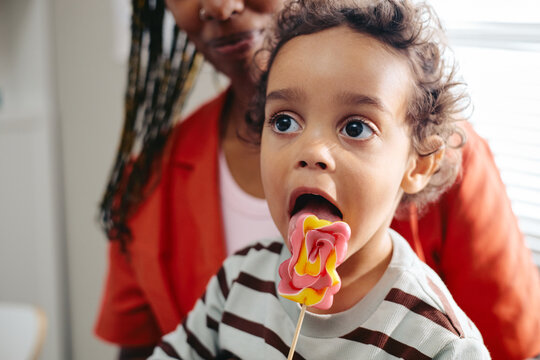 African American toddler child licking candy lollipop near mother during pediatrician visit, close up. Image useful for pediatric healthcare campaigns and parenting advice content