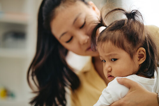 Asian young adult woman comforting Asian toddler girl during medical pediatric appointment. Visual suitable for pediatric healthcare campaigns and child wellness promotion