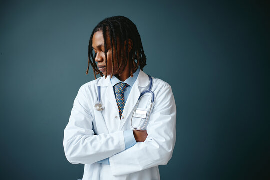 Young adult African American male pediatrician with stethoscope standing with arms crossed looking down thoughtfully. Image suitable for medical marketing campaigns and healthcare advertising