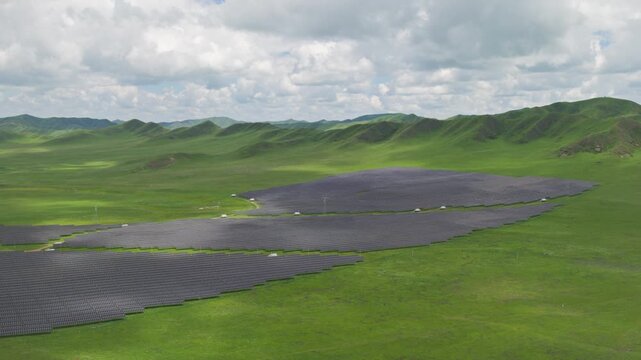 High-Angle Aerial View of Solar PV Panel Array on Zoige Grassland Mountains, Aba, Sichuan: Renewable Clean Energy, Agrivoltaics, Green Hills, Blue Sky and Cloud Background