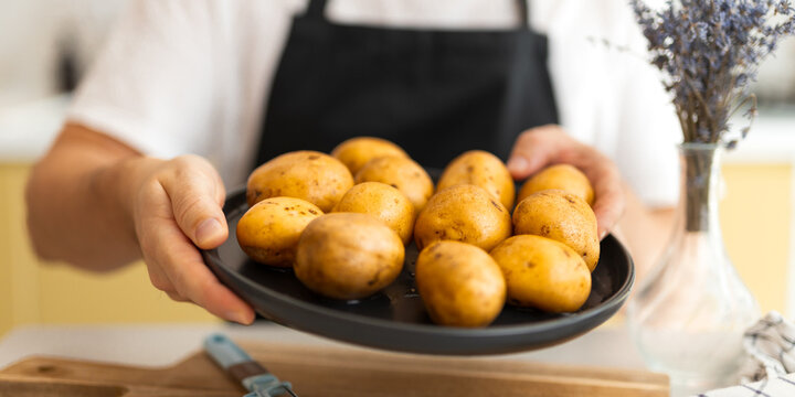 Person offering a plate of yellow potatoes toward camera in a kitchen for food background and farm to table banner design