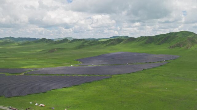 High-Angle Aerial View of Solar PV Panel Array on Zoige Grassland Mountains, Aba, Sichuan: Renewable Clean Energy, Agrivoltaics, Green Hills, Blue Sky and Cloud Background