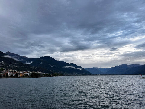 Dramatic view of locarno on lake maggiore with alpine mountains, waterfront buildings, low clouds and overcast sky in switzerland