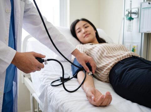 Patient undergoing a routine blood pressure check while resting on a hospital examination bed, medical worker operating a manual cuff and stethoscope to monitor cardiovascular vital signs, blood press