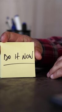 A vertical, slow-motion shot of hands holding a sticky note with a motivational message about self-improvement: &ldquo;Do it now.&rdquo;