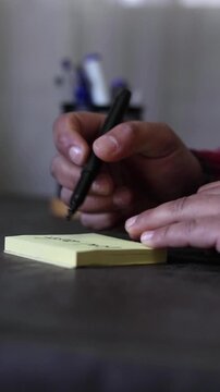 Vertical view of a person's hands writing the message &ldquo;Low cost&rdquo; on a sticky note on a desk