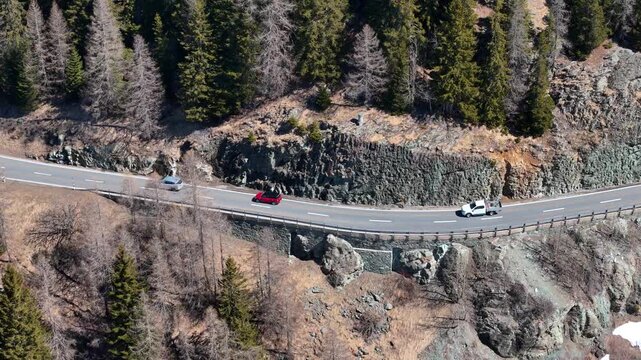 stone clad snow shed marks julier pass rest area campervan motorcyclists gather roadside switchback road winds through pine forest past rocky outcrops aerial drone footage graubunden switzerland
