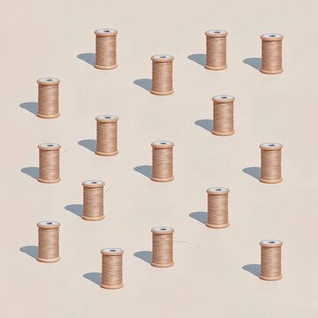 Waxed thread spools in a repetitive pattern, featuring matte khaki tones on a soft clay beige background for textile and craft projects