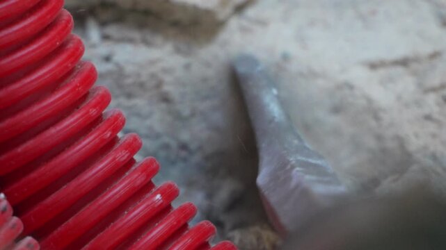 Heavy construction demolition tool chipping away at concrete floor next to a bright red corrugated tube. Close-up shot.