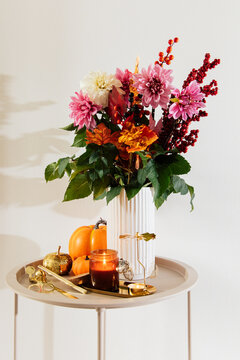 Flowers and autumn decorations on a round table near a wall with a neutral color
