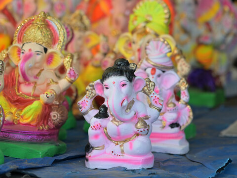 A small, beautifully painted white and pink Lord Ganesha idol displayed prominently among a colorful collection of idols for the Ganesh Chaturthi festival.