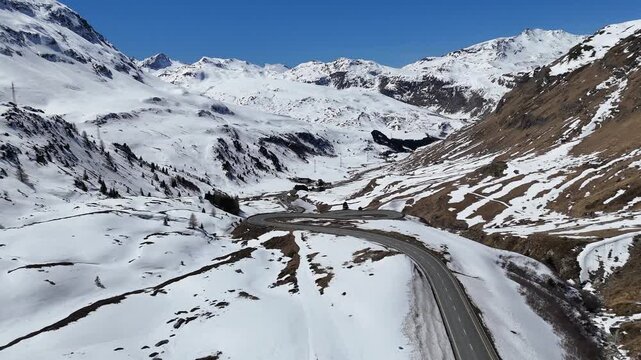 winding alpine road traces gentle curve across snowbound slope toward rocky outcrop julier pass mountain crossing graubunden switzerland high altitude route linking engadin valley chur st moritz