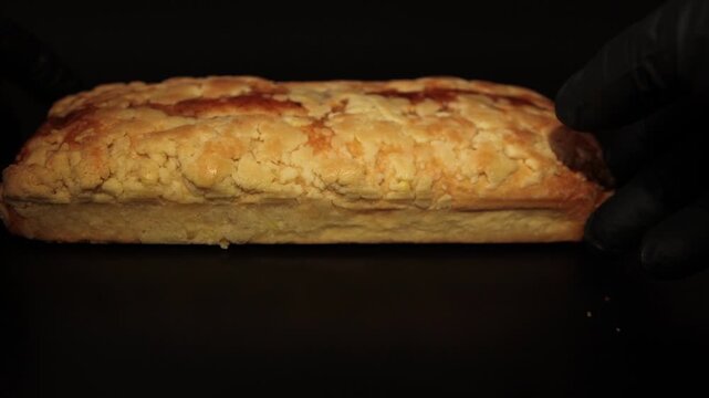 Close-up shot of a pastry chef in black gloves placing and adjusting a freshly baked hazelnut loaf cake on a dark surface. Perfect stock video for bakery ads, culinary tutorials, and dessert packaging
