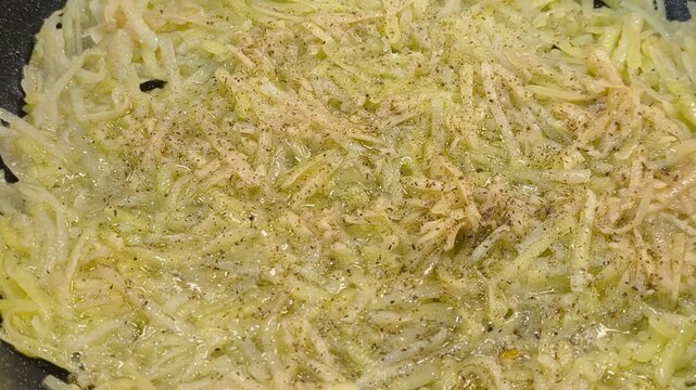 Large grated potato fritter cooking in a frying pan. Hot oil bubbles around the potato pancake as a golden crispy crust forms during frying. Homemade potato pancake made from coarsely grated potatoes.