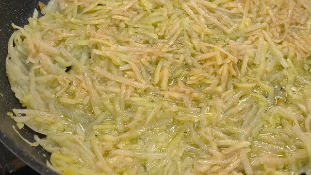 Large grated potato fritter cooking in a frying pan. Hot oil bubbles around the potato pancake as a golden crispy crust forms during frying. Homemade potato pancake made from coarsely grated potatoes.