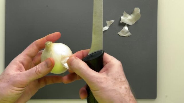 Close up hands peeling slicing onion over dark cutting board under studio lighting emphasizes texture skin layers culinary prep mood with scattered peels and glossy surface detail