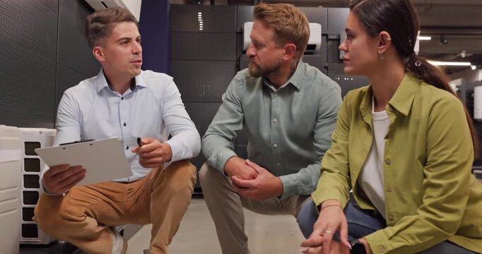Salesman consultation couple choosing shopping airconditioner retail store. Expert advisor shares advice with clipboard, comparing split and portable units for customers. AC buy tips for homes.