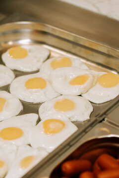 Fried eggs cooking on a large metal commercial griddle for a breakfast service in the morning