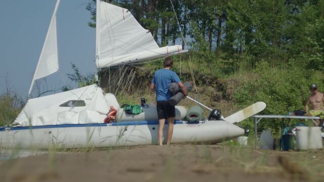 Family with kids sailing on the lake during sunny summer day and unloads the boat beached on the coast