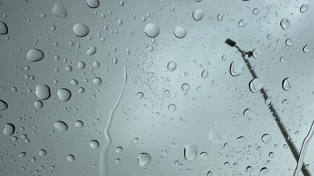 Static shot of heavy rain on a parked car windshield with raindrops and a streetlight outside.
