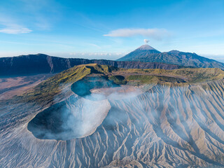 Aerial daylight panorama of Mount Bromo vast volcanic caldera, rugged ridges, crater terrain, and distant smoking peak. © Cloudyew