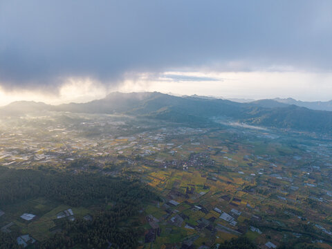 Misty dawn bathes rolling hills and valley town. Sunlight breaks through clouds at Pronojiwo, Lumajang