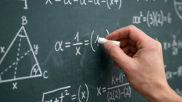 Student in casual clothing writing mathematical equations on classroom blackboard with chalk